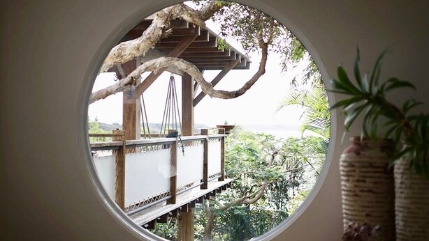 A circular window with a view of a wooden deck and a tree. - Haven Oceana (Emerald Beach)