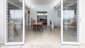 A spacious interior with a central dining area, a fireplace, and large glass doors leading to an outdoor deck. - Haven Oceana (Emerald Beach)
