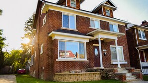A two-story brick house with a front porch, large windows, and a visible address number. - 6 Bedroom/4.5 Bath/Across from Motown Museum (Detroit)