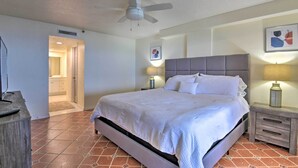 A bedroom with a bed, nightstands, a ceiling fan, and a door leading to a bathroom. - Beachfront Resort Condo w/ Panoramic Ocean Views! (New Smyrna Beach)