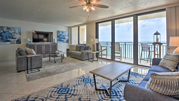 A spacious living room with a large window overlooking the ocean, a ceiling fan, and a flat-screen TV. - Beachfront Resort Condo w/ Panoramic Ocean Views! (New Smyrna Beach)