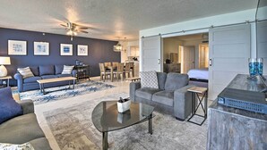 A modern living room with a ceiling fan, a sofa, a coffee table, and a dining area with chairs and a table. - Beachfront Resort Condo w/ Panoramic Ocean Views! (New Smyrna Beach)