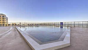 A rectangular pool with a concrete border, surrounded by a metal railing, and a clear sky in the background. - Beachfront Resort Condo w/ Panoramic Ocean Views! (New Smyrna Beach)