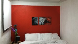 Un dormitorio con pared roja, una cama con ropa de cama blanca y dos cuadros encima de la cama.