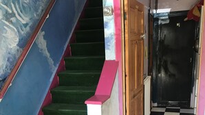Una escalera con alfombra verde y barandillas rosadas, que conduce a un cuarto con piso a cuadros blanco y negro.
