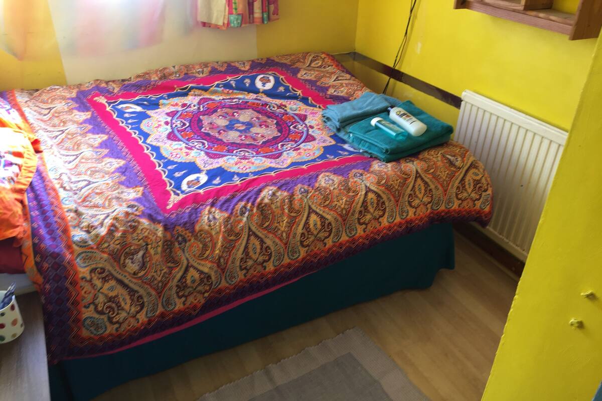 A bed with a colorful patterned bedspread, a folded towel, and a bottle on the side.