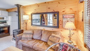 Interior acogedor de una cabaña con detalles de madera, un sofá con cojines estampados, una lámpara y un espejo que refleja la zona de la cocina.