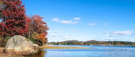 A calm lake with autumn foliage and distant hills.