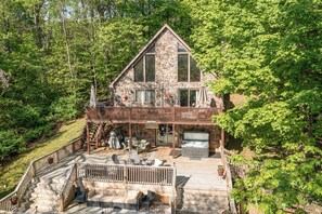 Escape to a serene cabin nestled in a forest, featuring a spacious deck with outdoor seating and a hot tub.