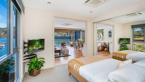 A modern bedroom with a large bed, a TV, and a balcony with a view of the water. - The Deckhouse, Cottage Point. Waterfront Adults Retreat. (Cottage Point)
