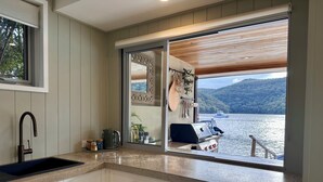 A kitchen with a view of a lake and mountains, featuring a sink, cabinets, and a grill. - The Deckhouse, Cottage Point. Waterfront Adults Retreat. (Cottage Point)
