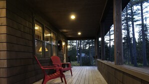 Une terrasse en bois avec deux chaises rouges, un bâtiment en bois doté de grandes fenêtres et une vue sur de grands arbres.