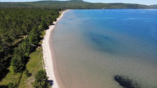 Une vue aérienne d’une plage au rivage bien défini, entourée d’une forêt dense et avec des collines en arrière-plan.