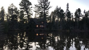 Une cabane entourée de grands arbres et bordant un lac paisible.