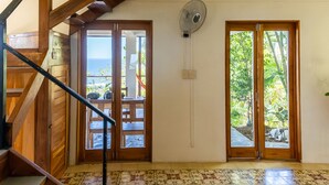 Una habitación amplia con una escalera de madera, dos puertas correderas de cristal que dan a un balcón y un ventilador de techo.