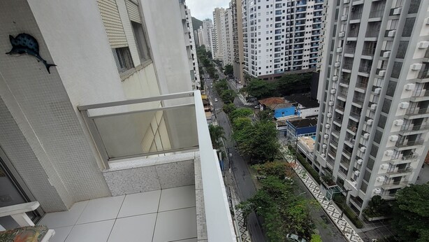 Un edificio residencial alto con balcón, piso de baldosas y vista a la calle con coches y zonas verdes.
