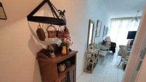 Un pasillo con un armario de madera, un perchero metálico y un comedor al fondo.