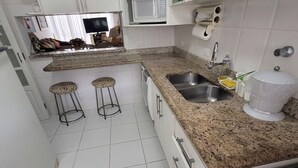 Cocina con armarios blancos, encimera de granito, dos taburetes, microondas, fregadero y estufa.