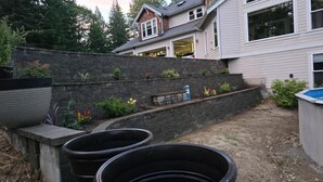 Un patio trasero residencial con un muro de contención de piedra, una jardinera de concreto y una piscina.
