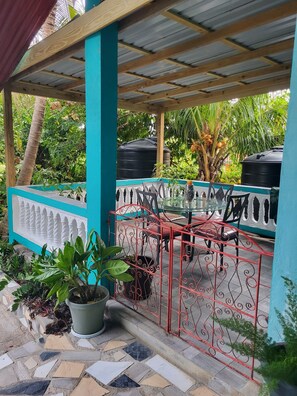 A covered outdoor seating area with a tiled floor, metal railing, and potted plants.