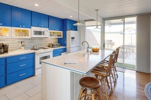 Een moderne keuken met blauwe kastjes, witte aanrechtbladen en een centraal eiland met barkrukken.