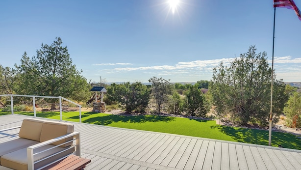Une terrasse en bois avec un canapé et un banc, donnant sur une pelouse bien entretenue et des arbres.