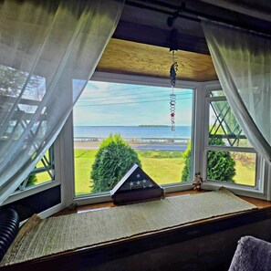 A room with a large window, a view of a body of water, and a small American flag on the windowsill.