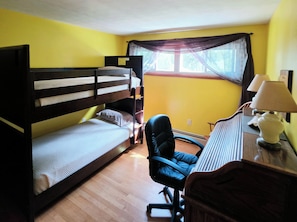 A room with a bunk bed, a desk with a lamp, a chair, and a window with curtains.