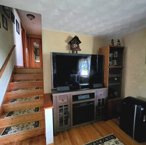 Un salon avec un escalier, un téléviseur à écran plat, des meubles en bois et une horloge au mur.