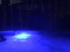 Une pièce faiblement éclairée, avec une source de lumière bleue sur le sol, un mur orné de motifs et des guirlandes lumineuses.