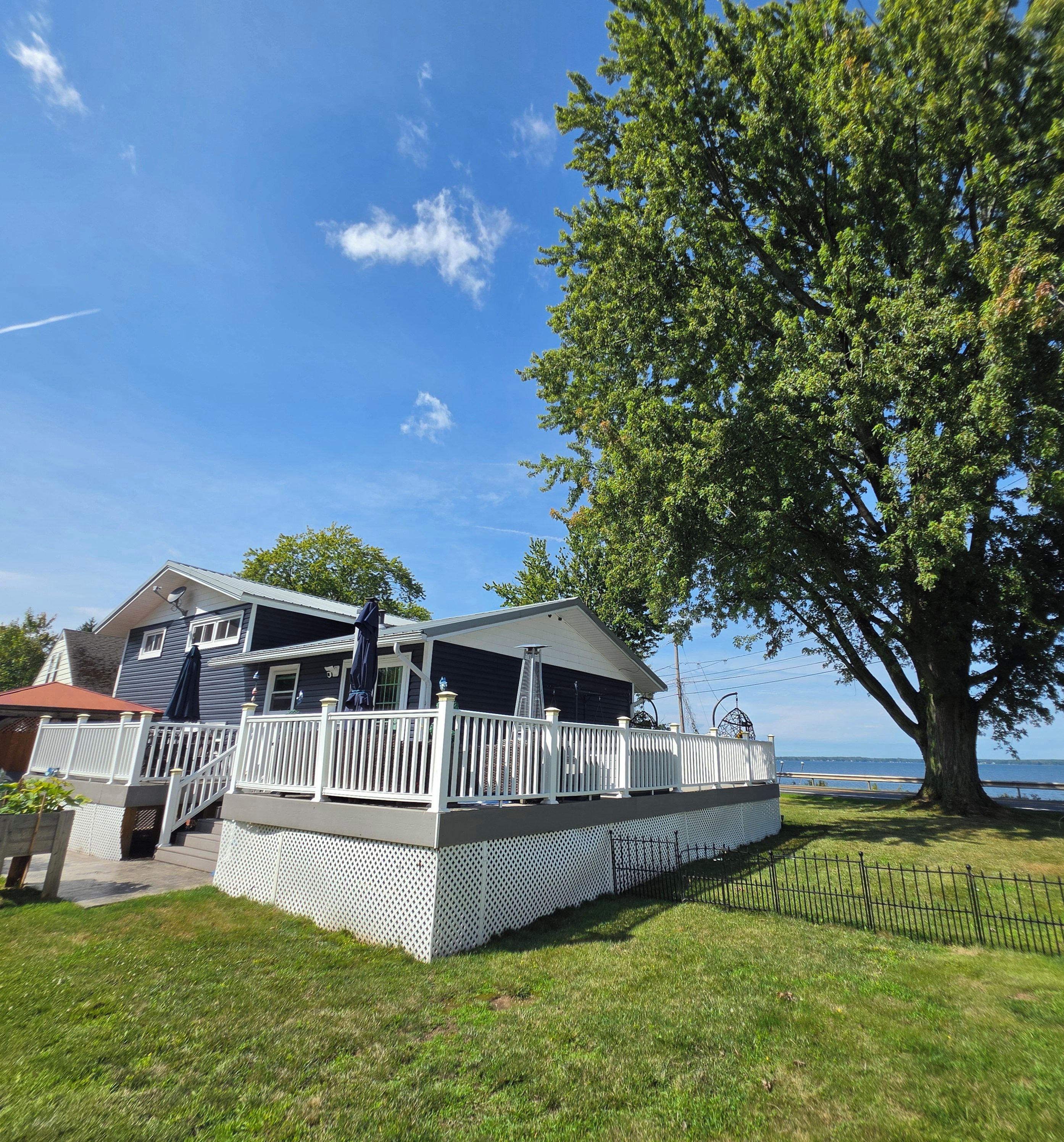 A two-story house with a deck, a large tree, and a view of the water.