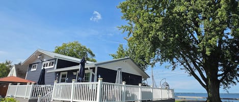A two-story house with a deck, a large tree, and a view of the water.