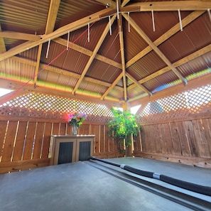 A room with a sloped ceiling, wooden walls, a central table, and a hanging plant.