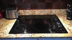 Una cocina con placa de inducción negra, un tostador de acero inoxidable y un bloque de cuchillos.
