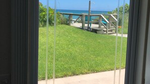 Vista a través de un ventanal a un patio con piscina, césped verde y terraza de madera.