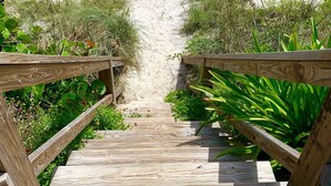 Un muelle de madera que conduce a una playa arenosa con olas al fondo.