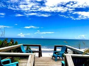 A wooden deck with two blue chairs facing the ocean.