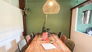 Ein Holzesstisch mit einer gewobenen Pendelleuchte, umgeben von Stühlen. Eine kleine Topfpflanze hängt an der Wand, und auf dem Tisch ist eine Flasche zu sehen.
