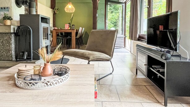 Eine moderne Küche mit Einbauherd, Essbereich mit Tisch und Stühlen, ein bequemer Sessel und ein Fernseher auf einem Schrank.