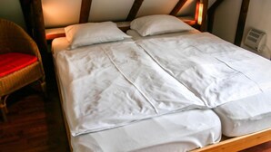 Ein Schlafzimmer mit hölzernem Bettgestell, weißer Bettwäsche und einem Korbstuhl mit rotem Kissen.