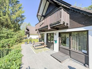 Un bâtiment moderne doté d’une façade en bois, de grandes fenêtres et d’un espace extérieur pavé avec un banc.