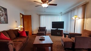 Een hotelkamer met een plafondventilator, een flatscreen televisie, een bank, een bijzettafeltje en een lamp.