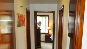 Een gang met houten vloer en deuren die leiden naar een kamer met een lamp en een ventilator.