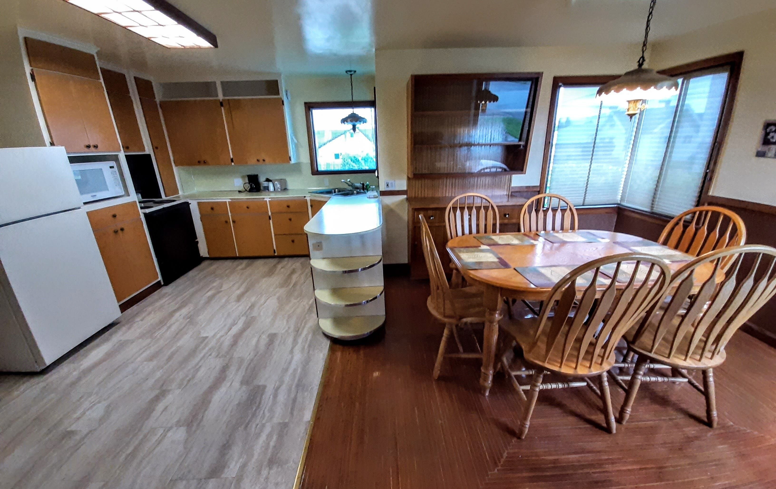 A compact kitchen with wooden cabinets, a built-in microwave, and a dining area with a wooden table and chairs.