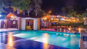 Ein Poolbereich mit einem Gebäude, das eine überdachte Terrasse und Sitzmöglichkeiten im Freien bietet.