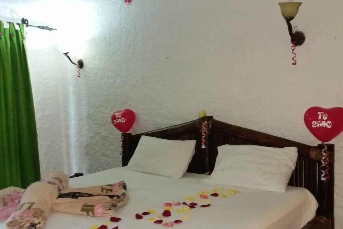 A bed with rose petals and heart-shaped balloons, a green curtain, and a wooden headboard.