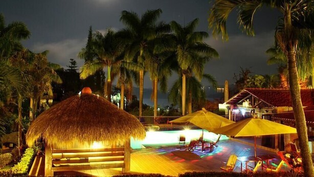 Ein Resort bei Nacht mit Poolbereich, Palmen und einer Struktur mit Reetdach.