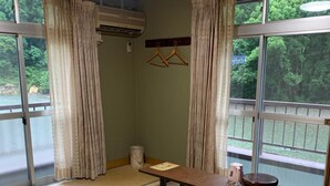 A tatami mat room with a low table, a hanging air conditioner, and a view of a forested area. - Kawayu onsen Minshuku SUMIYA (Tanabe)