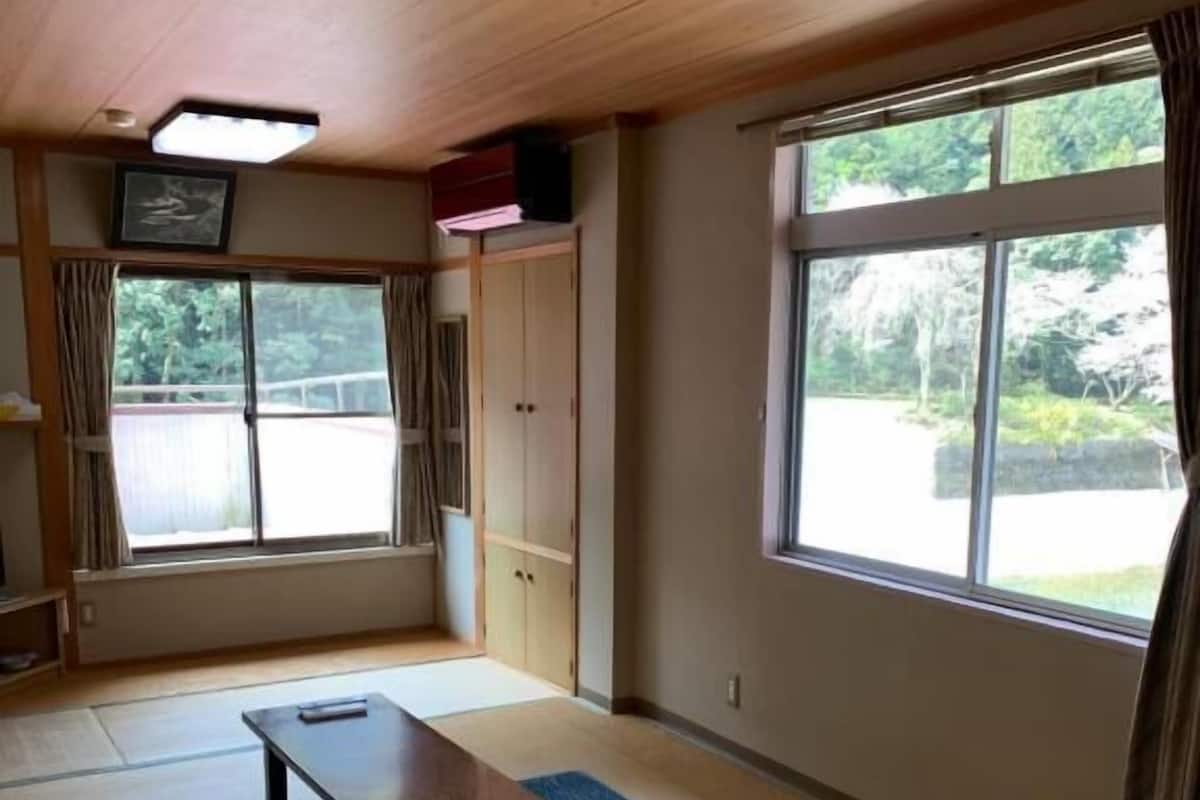 A room with tatami flooring, a low table, a cabinet, and large windows with curtains.