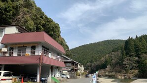 A building with a red roof and a balcony, adjacent to a river with a wooden walkway. - Kawayu onsen Minshuku SUMIYA (Tanabe)